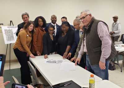 Group of people standing in a group, around a table looking at architectural plans and smiling.