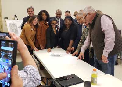 Group of people standing in a group, around a table looking at architectural plans and smiling.